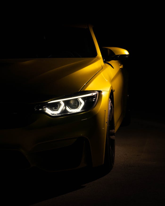 A striking yellow sports car captured with headlights on in moody low light setting.